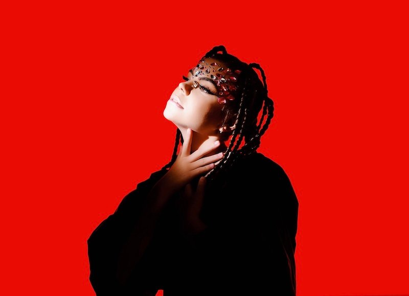 Alessiah - "Darling" press photo with lots of gems covering her forehead; she's standing in front of a red background