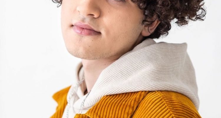 Issam Alnajjar press photo wearing a white hoodie and brownish jacket