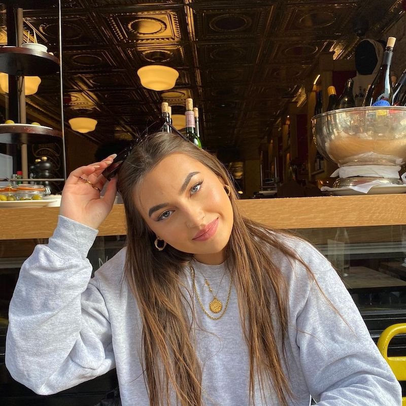 Gigi Moss press photo wearing a grey sweatshirt while seated inside an eatery 