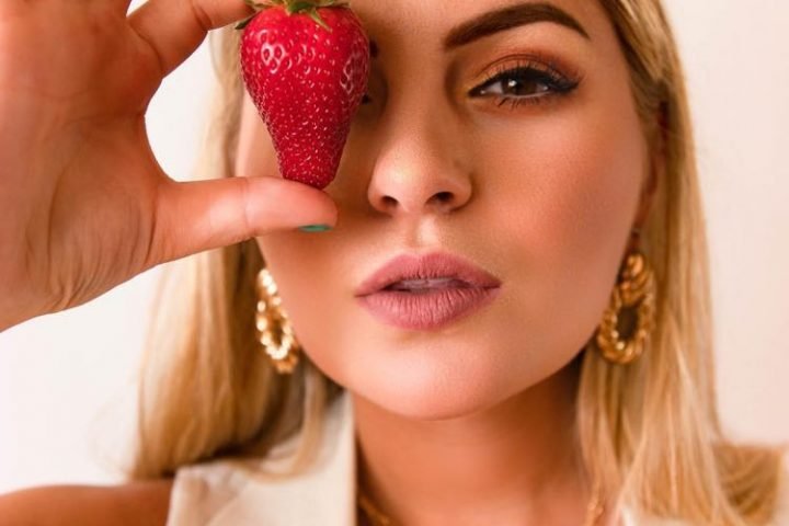 Taylor Tote press photo holding a strawberry over her right eye