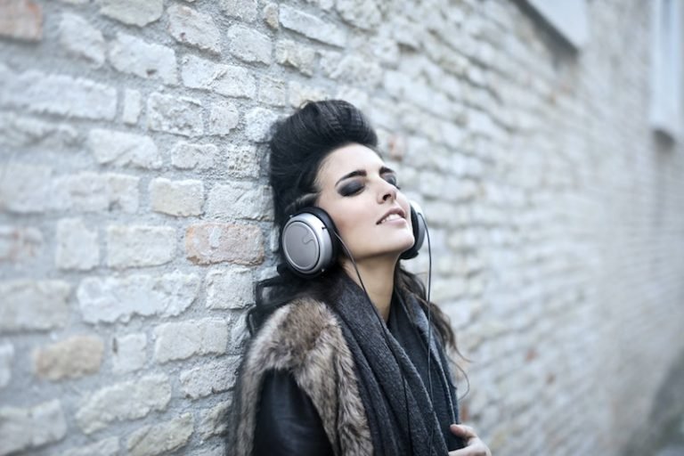 Young woman listening to music near grunge wall