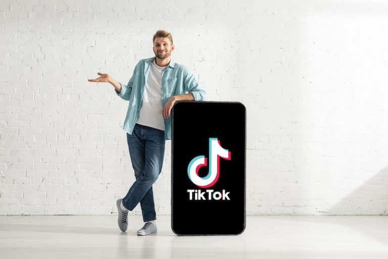 Smiling man showing confused gesture near big model smartphone with TikTok app — Photo by HayDmitriy